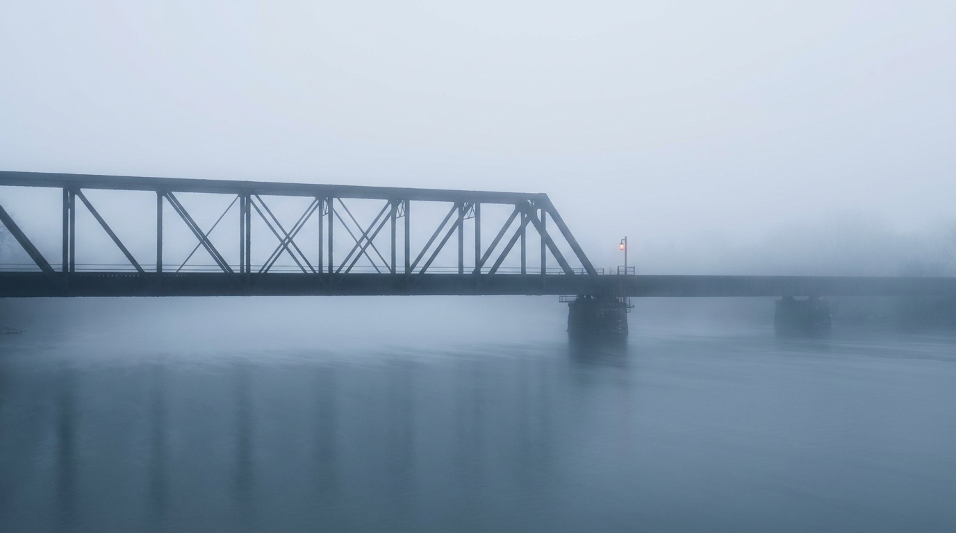 A steel truss bridge over a river in morning fog